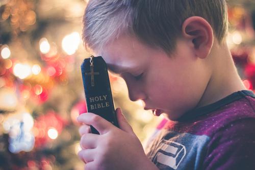 Criança rezando com a Bíblia